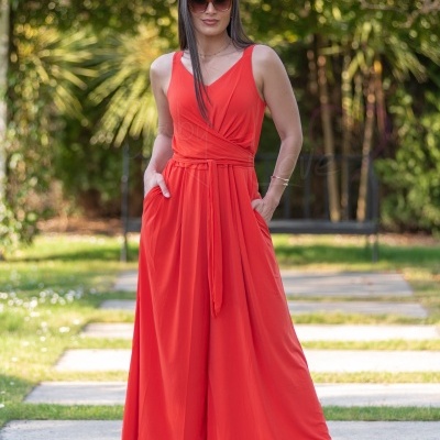 Macacão vermelho comprido com alças largas e cinto, usado por mulher junto a relva e árvores.