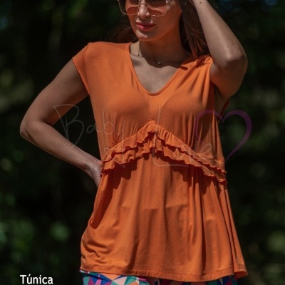 Mulher com túnica laranja e calças coloridas em ambiente exterior