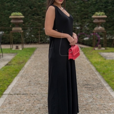 Mulher com vestido preto comprido, sapatos rosa e mala rosa em caminho de pedra