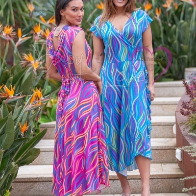 Duas mulheres vestem vestidos midi com padrões ondulados coloridos em escadas exteriores com plantas tropicais