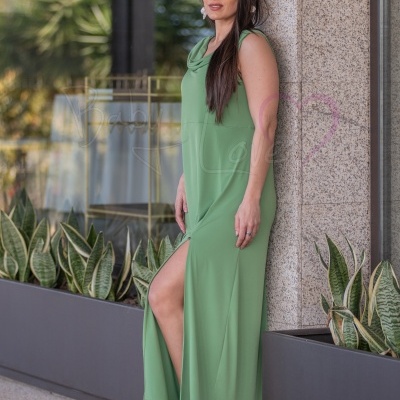 Mulher com vestido verde e sandálias de salto junto a plantas e parede de pedra