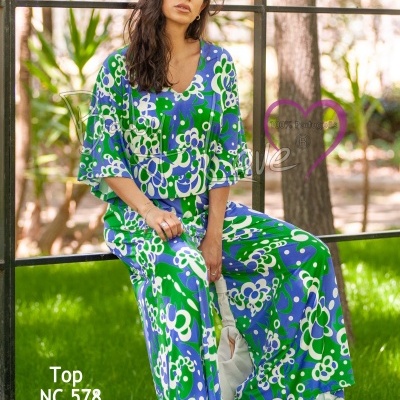 Mulher sentada com conjunto floral verde, azul e branco, top e pantalona, ambiente exterior com árvores e relva