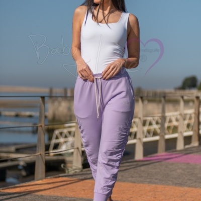 Mulher a usar calças lilás com cordão branco e top branco sem mangas exterior perto do mar.