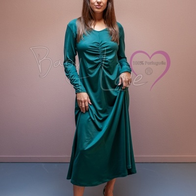 Mulher com vestido comprido verde esmeralda e sapatos verdes, parede rosa claro