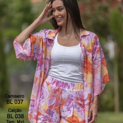 Conjunto camisa e calção florais coloridos com fundo roxo, laranja e amarelo usados por mulher sorridente ao ar livre.