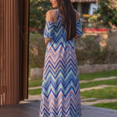 Vestido comprido geométrico azul e branco, corte ombro descoberto, mulher em ambiente exterior.