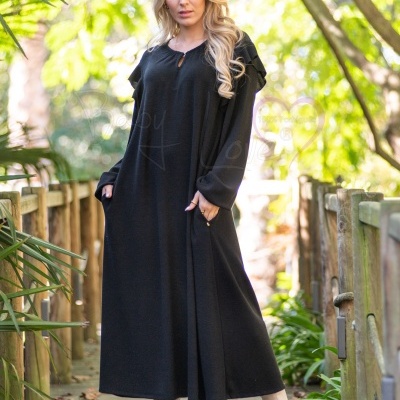 Vestido comprido preto com folhos nos ombros e botas brancas num passadiço exterior