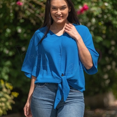 Mulher com camisa azul de tecido leve e nó na frente e jeans azul claro ao ar livre