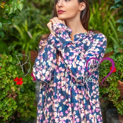 Vestido comprido de mangas compridas com padrão floral azul, rosa e branco, mulher com fundo de vegetação