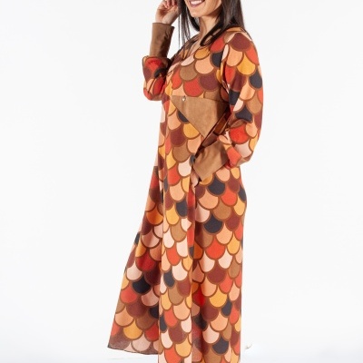 Mulher com vestido de padrão castanho, laranja e bege, botas castanhas e chapéu castanho