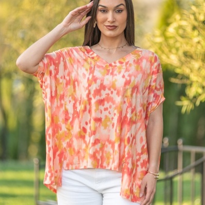 Blusa colorida em tons de laranja, amarelo e branco com calças brancas, ao ar livre