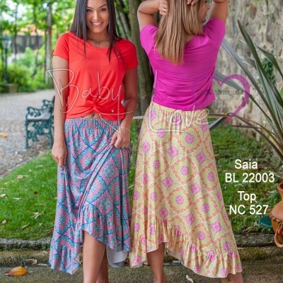 Duas mulheres ao ar livre vestindo tops vermelhos e rosas com saias compridas coloridas e com padrões geométricos.