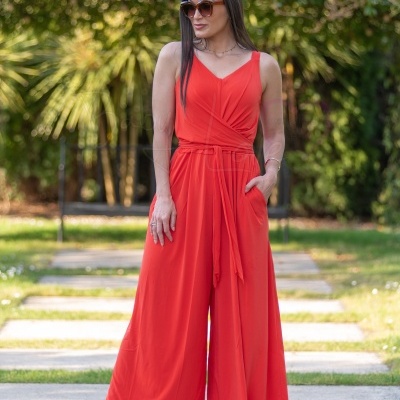 Macacão vermelho feminino longo com calça pantalona, ao ar livre e usando sandálias.