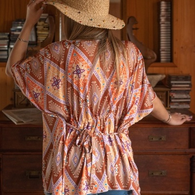 Blusa colorida de padrão geométrico e chapéu de palha em ambiente com mobília de madeira