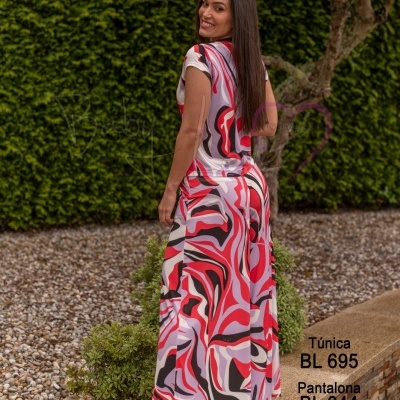 Mulher de costas com túnica e pantalona coloridas em jardim