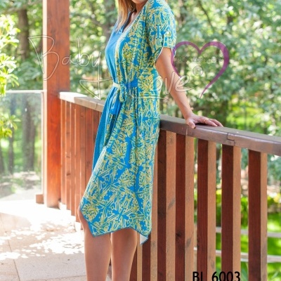 Vestido midi azul com padrão floral amarelo e cinto, salto alto transparente rosa claro, modelo em corredor de madeira com árvores ao fundo