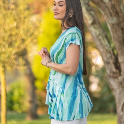 Blusa listrada azul e verde com mangas curtas e calças brancas em ambiente natural