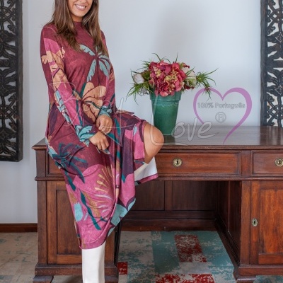 Vestido comprido floral com botas brancas junto a mesa de madeira e vaso com flores