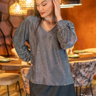 Mulher com túnica cinza brilhante e saia preta em ambiente rústico interior