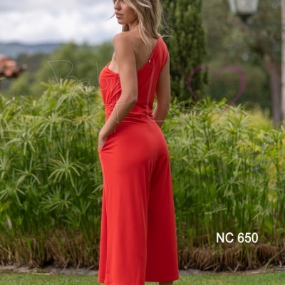 Mulher de costas a usar macacão vermelho com um ombro só num jardim verde.