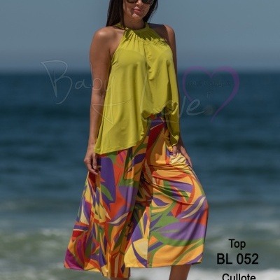 Mulher na praia com top amarelo esverdeado e culotes coloridos de padrão geométrico