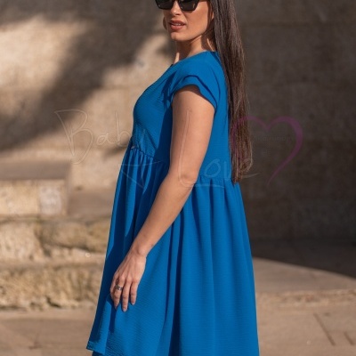 Vestido azul curto de tecido fluído com mulher de cabelo comprido e óculos pretos em ambiente exterior.