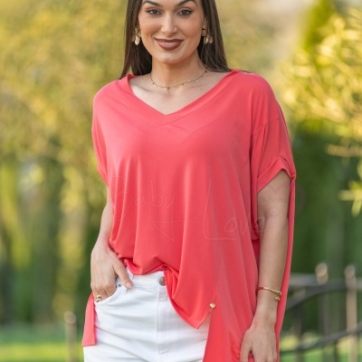 Mulher com blusa coral de decote em V e calças brancas em ambiente exterior