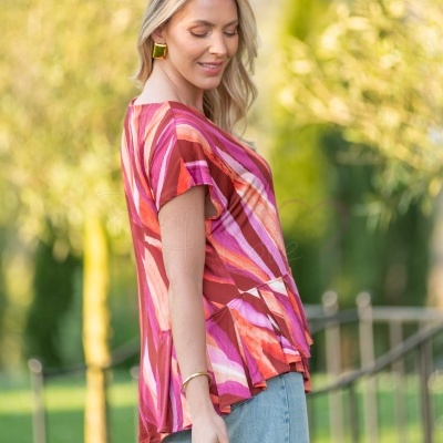 Blusa feminina rosa, vermelha e laranja com padrão abstrato e calças jeans claras
