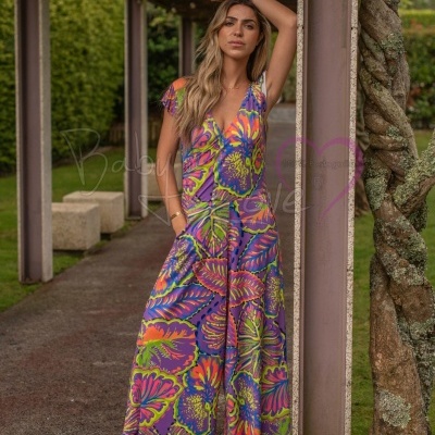 Vestido colorido comprido com padrão de folhas usado por mulher em ambiente exterior com pilares e árvore.