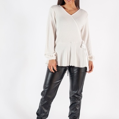 Mulher com camisola branca de malha, calças pretas de couro sintético e botas taupe