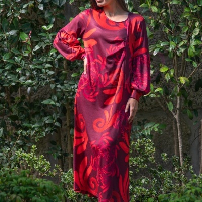 Vestido longo com padrão floral em vermelho e roxo usado por mulher em ambiente exterior com plantas