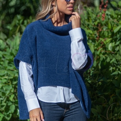 Mulher a usar capa azul e camisa branca com calças jeans ao ar livre