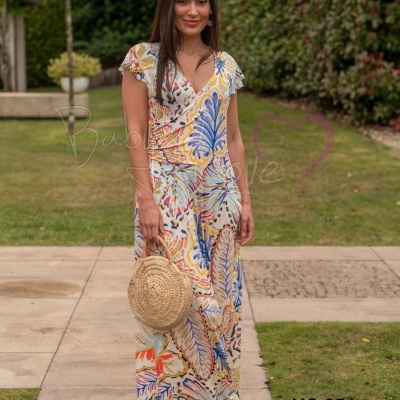 Mulher usando vestido comprido colorido com padrões florais e segurando bolsa redonda de palha
