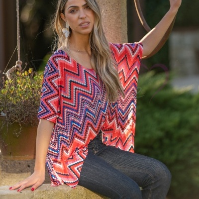 Mulher com blusa colorida padrão zig-zag e calças jeans sentada ao ar livre
