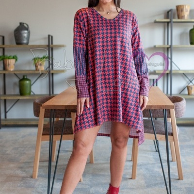 Vestido curto de malha com padrão pied-de-poule em tons de vermelho e preto, mangas longas e corte assimétrico, combinado com botins vermelhos, cenário interior com móveis de madeira e plantas.