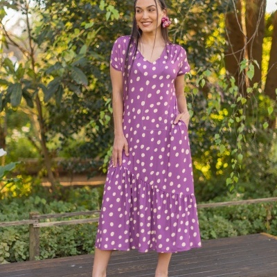 Vestido roxo de bolinhas brancas com decote em V e babado na saia, usado por mulher ao ar livre