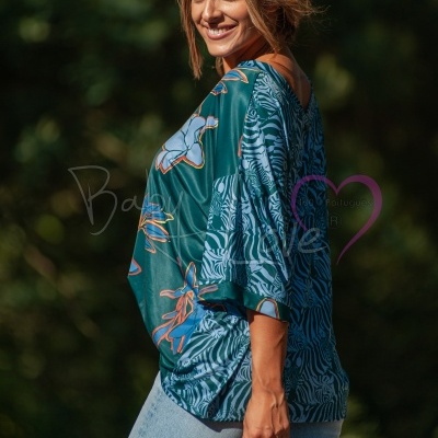 Mulher veste blusa verde com padrões florais e calças jeans claras em ambiente natural