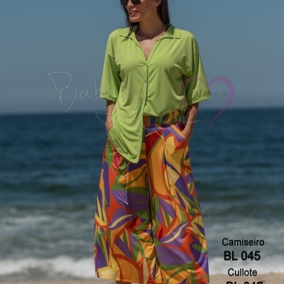 Mulher na praia com camisa verde e calças pantalona coloridas junto ao mar