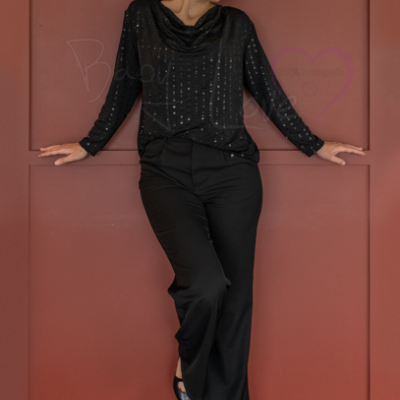 Mulher com blusa preta brilhante e calças pretas em frente a parede vermelha