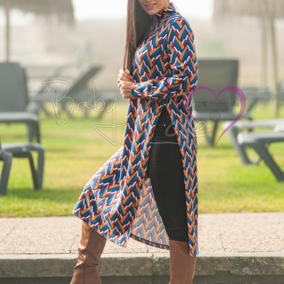 Mulher com vestido comprido geométrico azul, laranja e branco, leggings pretas e botas castanhas num espaço exterior.