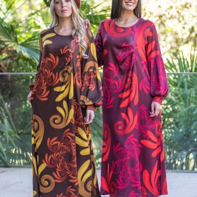 Duas mulheres com vestidos compridos florais em ambiente com plantas tropicais