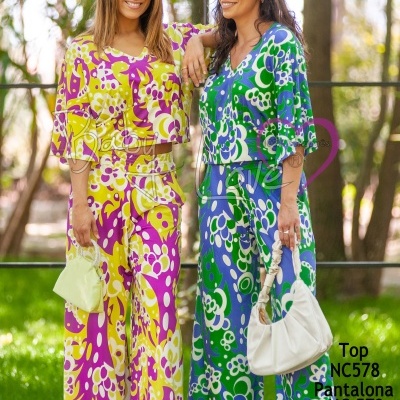 Duas mulheres em roupa colorida com padrões florais, cada uma segurando uma mala em ambiente exterior