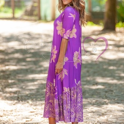 Vestido comprido roxo com flores bege, usado por mulher em exterior com árvores