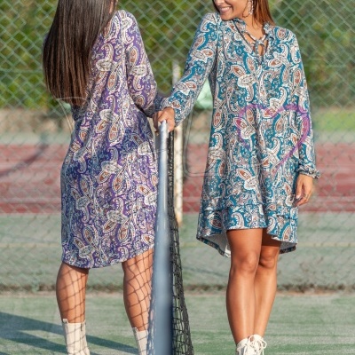 Duas mulheres com vestidos de padrão em campo de ténis junto a uma rede