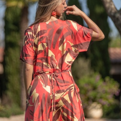 Vestido longo vermelho com padrão floral e cinto fino visto de costas ao ar livre