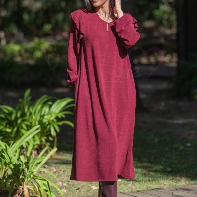 Vestido comprido vermelho com folhos e botas roxas em passadiço de madeira ao ar livre
