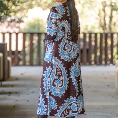 Veste comprida com padrão floral azul e branco sobre fundo castanho em ambiente exterior