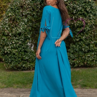 Mulher de vestido azul turquesa comprido com laços nas mangas ao ar livre