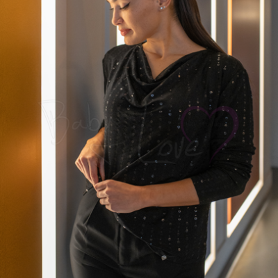 Mulher com blusa preta de manga comprida com lantejoulas e calças pretas num corredor iluminado