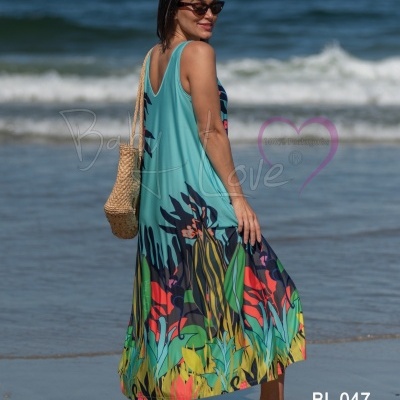 Mulher na praia com vestido longo colorido e bolsa de palha, vista lateral